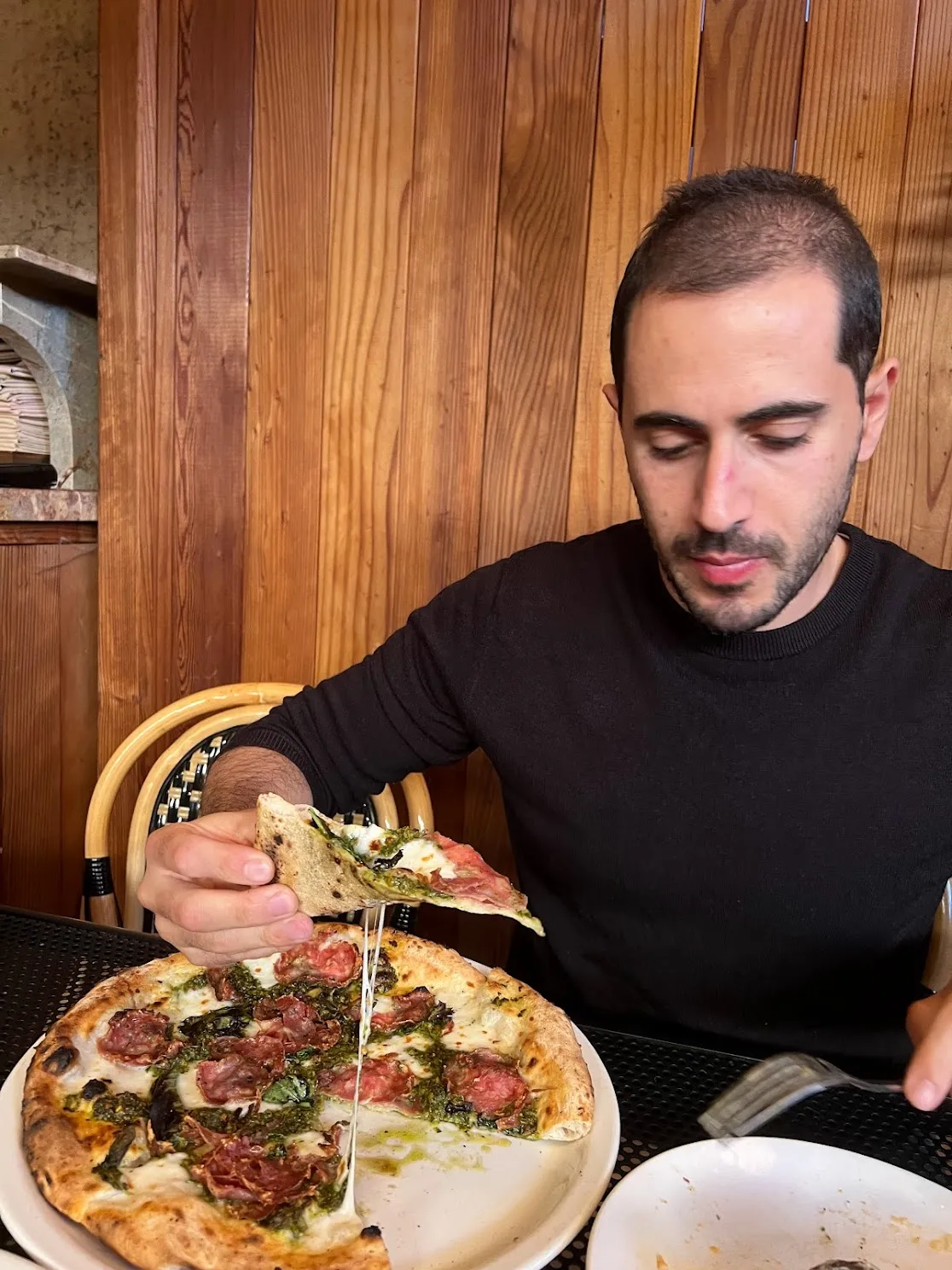 Mahdi enjoying pizza with salami and pesto at a restaurant