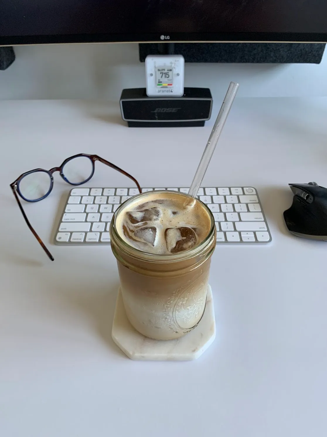 Iced latte in a mason jar on desk with keyboard and monitor