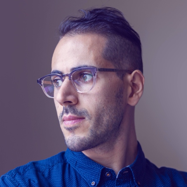 Mahdi Farra in glasses and a blue dotted shirt, looking to the side.